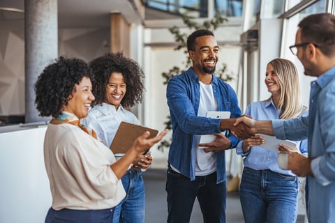 A diverse group of professionals smiling and shaking hands in a modern office environment.