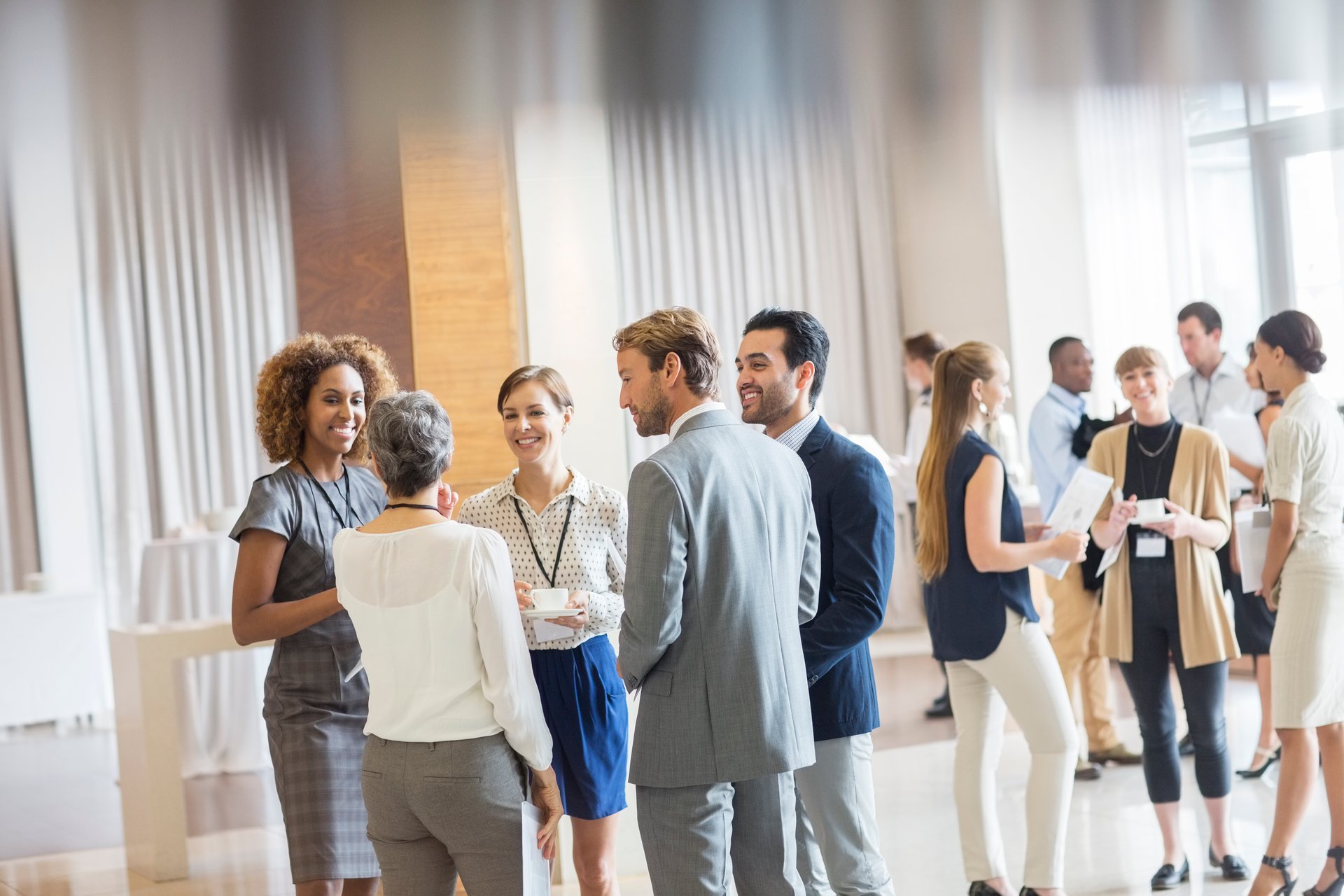 A diverse group of professionals networking and chatting at a business event in a bright, modern space.