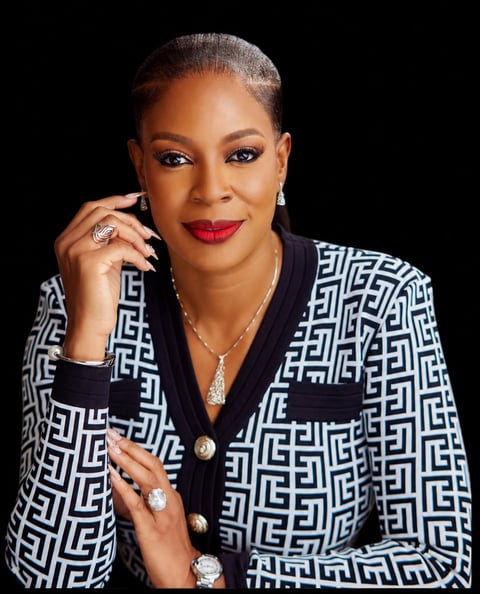 Professional portrait of a woman wearing a geometric patterned blazer with red lipstick, jewelry, and grey hair against a black background