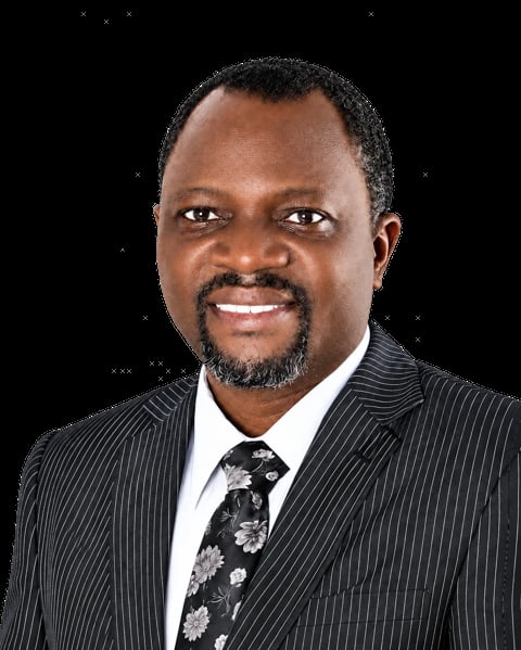 Professional headshot of a smiling man in a dark pinstriped suit, white dress shirt, and patterned tie against a black background