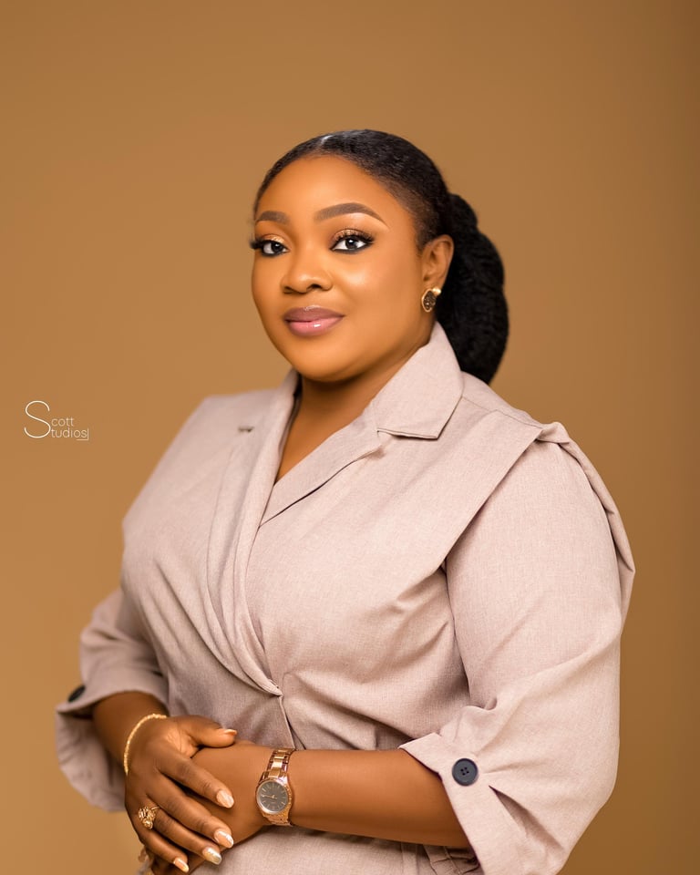 Professional headshot of a woman wearing a beige blazer against a tan background, with polished makeup and styled hair