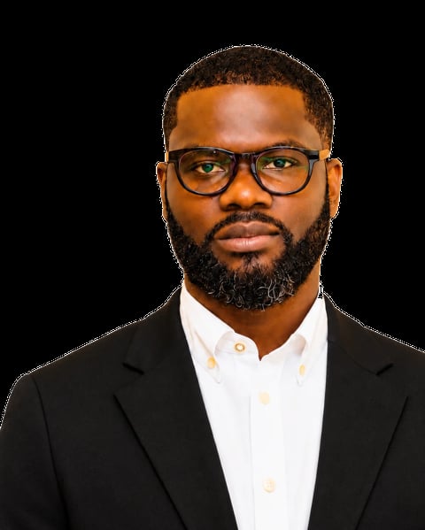 Professional headshot of a Black man wearing glasses, black blazer, and white shirt against a black background