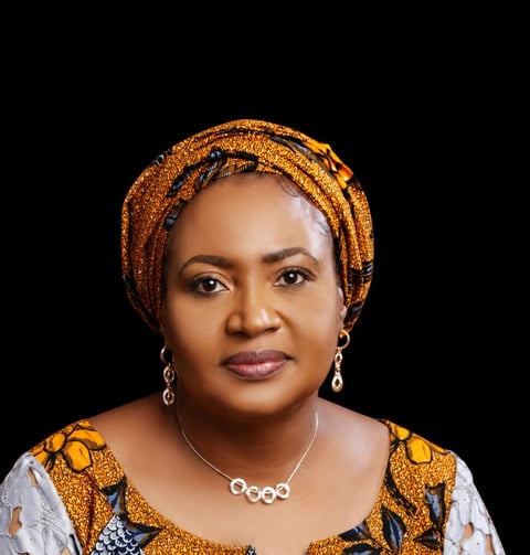Portrait of a woman wearing a gold patterned head wrap and matching clothing with a silver necklace against a black background