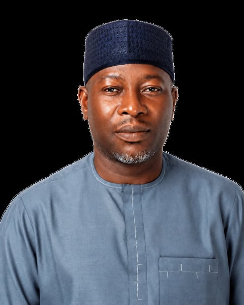 Professional headshot of a man wearing a blue traditional African robe and navy cap against a black background