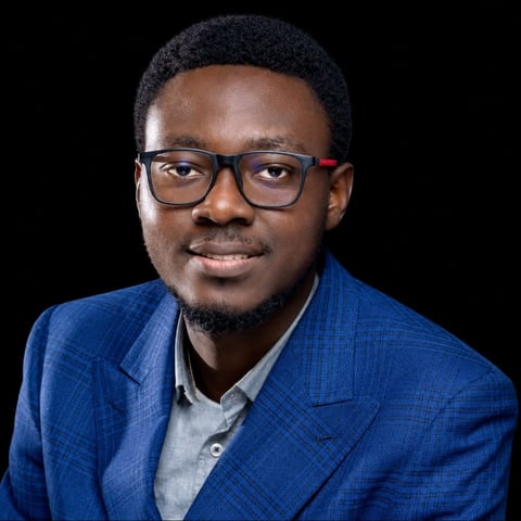 Professional headshot of a man wearing glasses and a blue blazer against a dark background