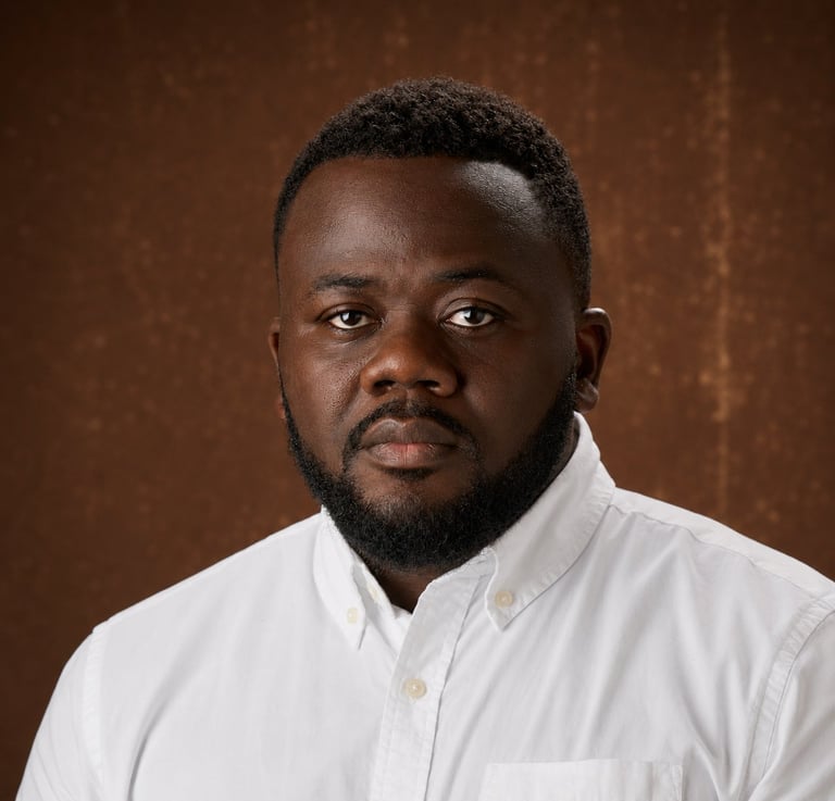 Professional headshot of a man with dark hair and beard wearing a white button-up shirt against a brown textured background