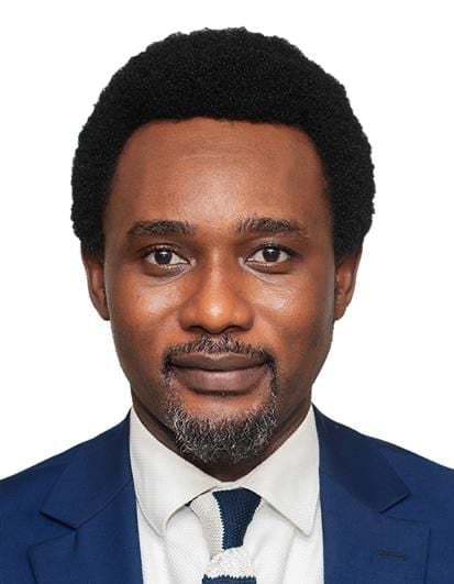 Professional headshot of a man wearing a dark blue suit jacket, white shirt, and dark tie against a white background