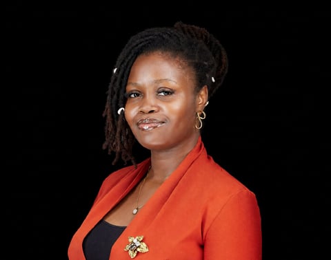 Professional portrait of a woman wearing a bright red blazer over a black top against a black background