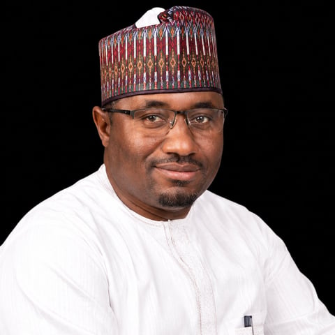 Portrait of a man wearing glasses, a burgundy patterned cap, and white traditional attire against a black background.